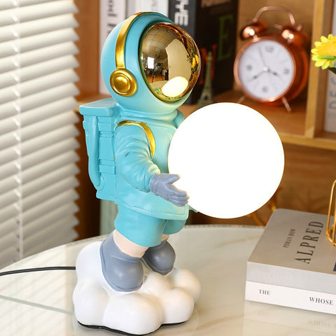 Astronaut Moon Lamp featuring astronaut in blue space suit holding moon in both hands. Astronaut Moon Lamp by Allthingscurated.