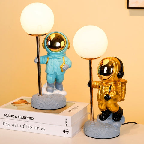 Two Astronauts in blue and gold space suit, each holding a pole with moon attached on top. Astronaut Moon Lamp by Allthingscurated.