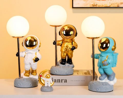 Three Astronauts in white, gold and blue space suit, each holding a pole with moon attached on top. Astronaut Moon Lamps by Allthingscurated.
