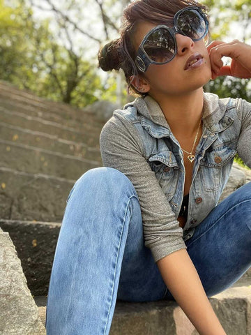 puerto rican woman sitting on staircase wearing denim vest and oversize sunglasses