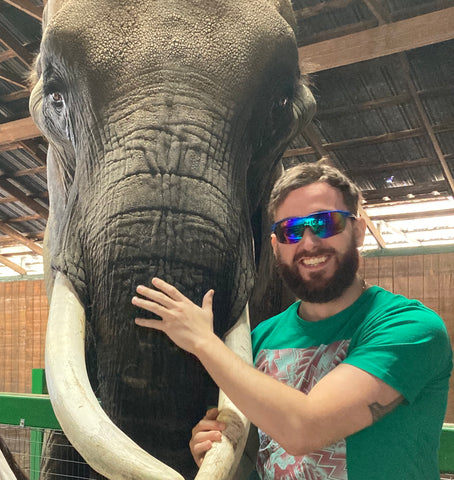 man wearing wrap around sunglasses while hanging out with elephant