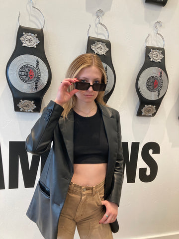 woman wearing leather jacket and black sunglasses standing in front of championship belts
