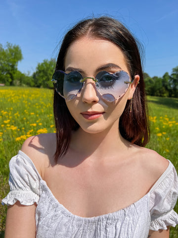 woman in a field of flowers wearing blue heart shape sunglasses
