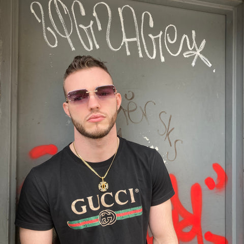 man wearing square sunglasses and gucci shirt standing in front of graffiti