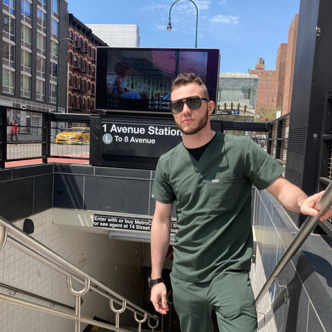man standing in subway entrance wearing scrubs and aviator sunglasses