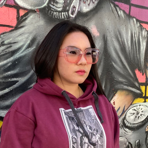 woman wearing burgundy hoodie and pink sunglasses standing in front of graffiti