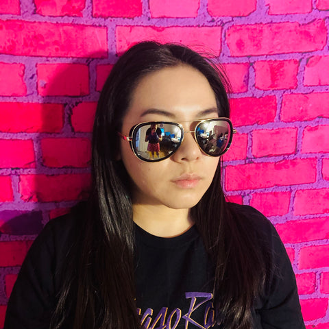 woman in front of pink backdrop wearing black t shirt and mirrored aviator sunglasses