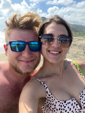 man and woman smiling on beach while wearing sunglasses