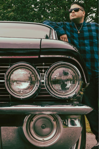 man standing next to a lowrider wearing a flannel and square sunglasses