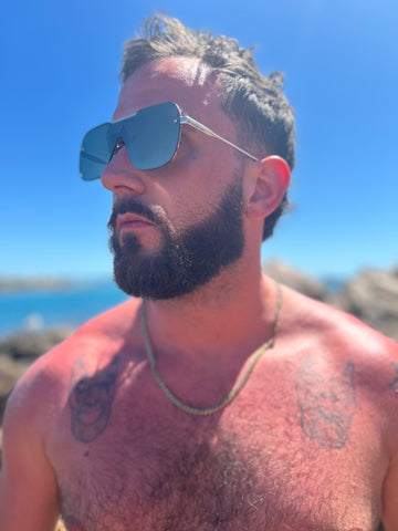 SUNBURNT MAN WITH BEARD WEARING AVIATOR SUNGLASSES ON THE BEACH