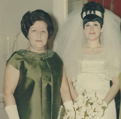 My grandmother is pictured here with her daughter, my mother, on her wedding day. My grandmother is wearing a green gown with white gloves. my mother is wearing her beautiful white wedding dress and is carrying her bouquet. Despite the happy occasion, she is not smiling. She was known to be a rather stoic woman.