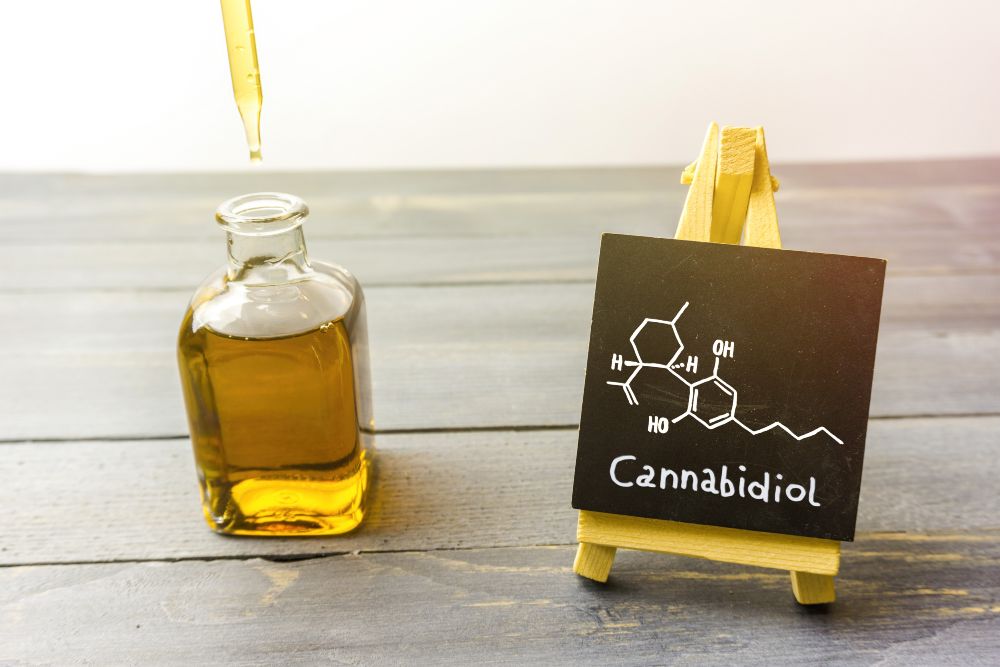 Cannabidiol, un frasco que contiene concentrado de CBD junto a un pizarrón donde se lee la composición química