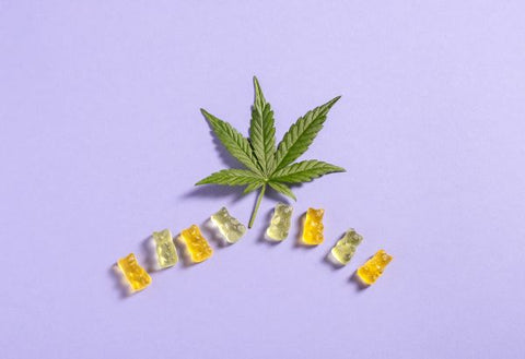 Hoja de cannabis junto a gomitas dulces en forma de ositos.