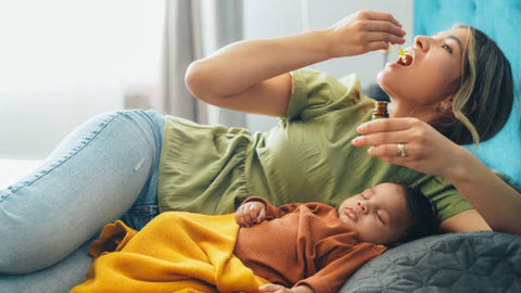 Mujer tomando gotas de CBD acompañada por su bebé en la cama.