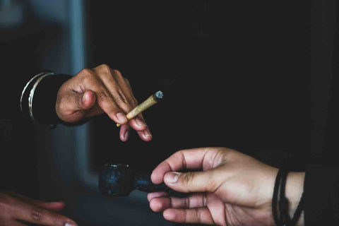 Two people passing a joint and pipe to one another 