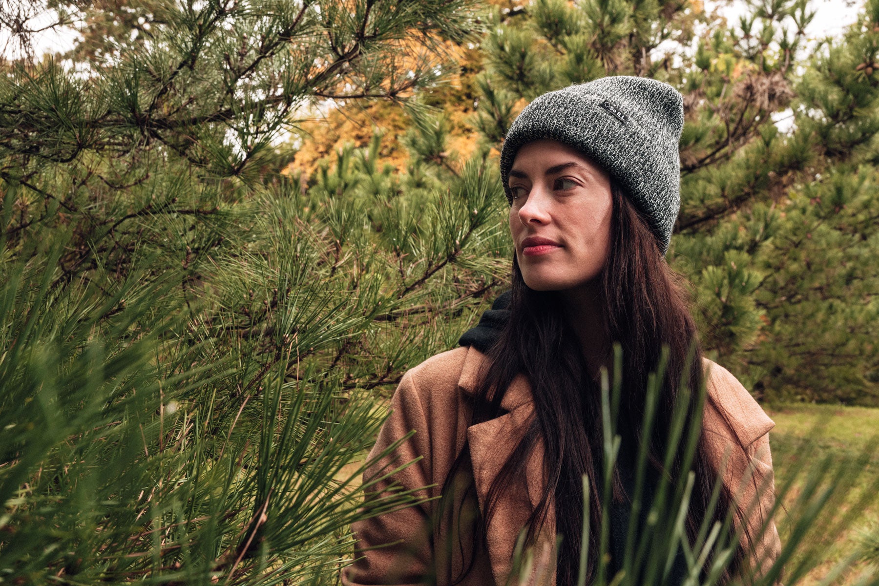 so ill heather beanie being worn by a woman in amidst some pine trees