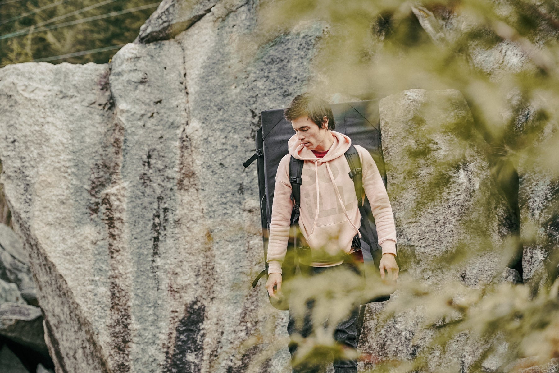 a man in the mountains carrying a climbing crash pad wearing a pink so ill hoodie