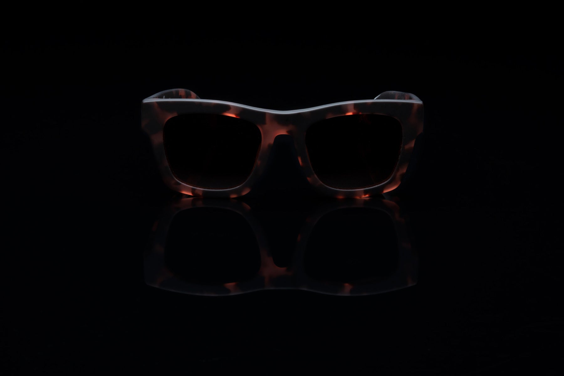 on the roam x electric matte rose tort sunglasses on a black reflective background