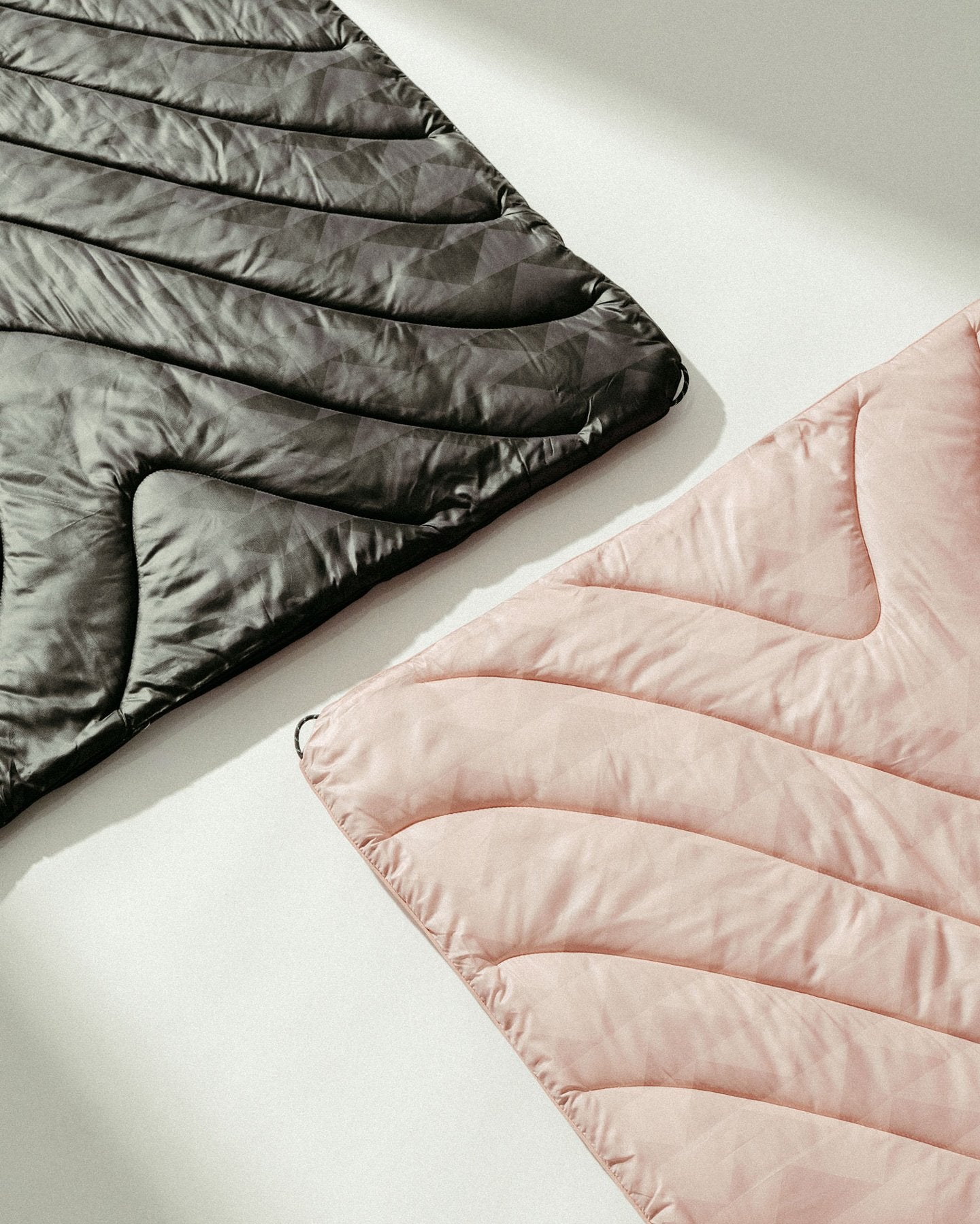 The Dirty Pink and Black Wolf Original Puffy Blankets from the Rumpl x So iLL x On The Roam, by Jason Momoa collaboration on a white surface, showcasing Jason Momoa's signature triangle pattern.