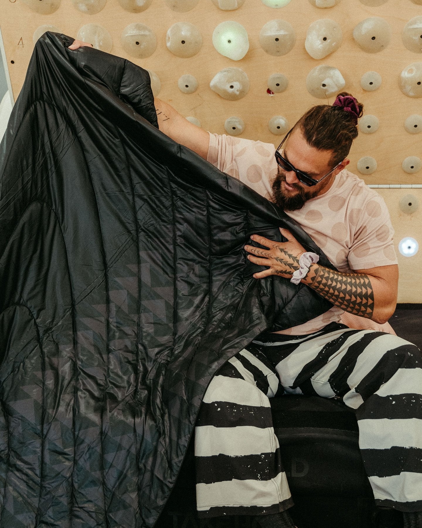 Jason Momoa holding up the Black Wolf Original Puffy Blanket from the Rumpl x So iLL x On The Roam, by Jason Momoa collaboration.