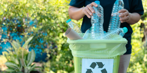 Hands placing plastic bottles into a recycling bin