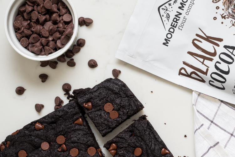 Black cocoa brownies next to a pouch of Modern Mountain Black Cocoa Powder