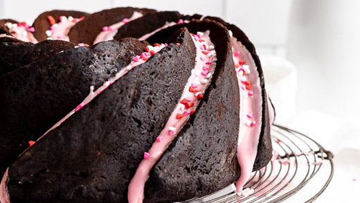A curved dark chocolate zucchini cake with pink frosting
