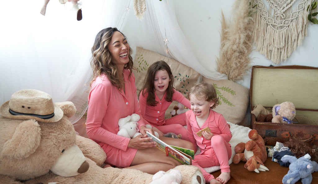 Family in matching blush beauty pink pajamas by Weekend Made reading a book in the kids room.