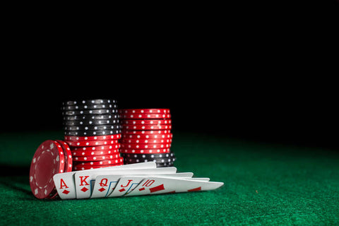 Stack of Texas Hold’Em Poker chips next to a hand of five cards on a poker table against a black background.