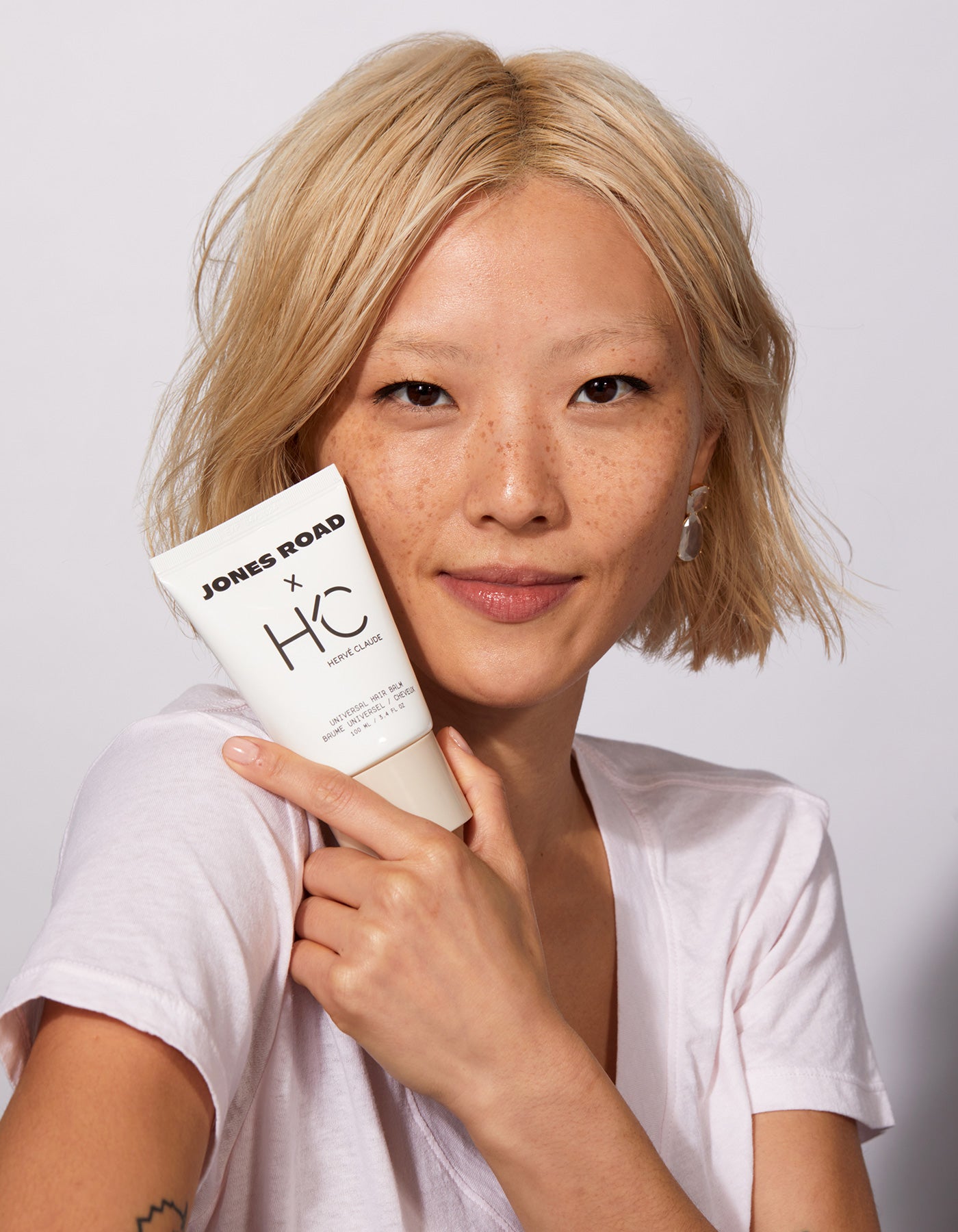 A woman holding The Universal Hair Balm by Jones Road Beauty