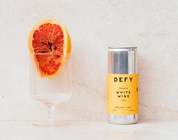 Glass with half a squeezed grapefruit next to a can of DEFY white wine.