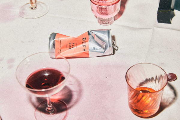DEFY crushed aluminium wine can that is 100% recyclable on a table next to some wine glasses