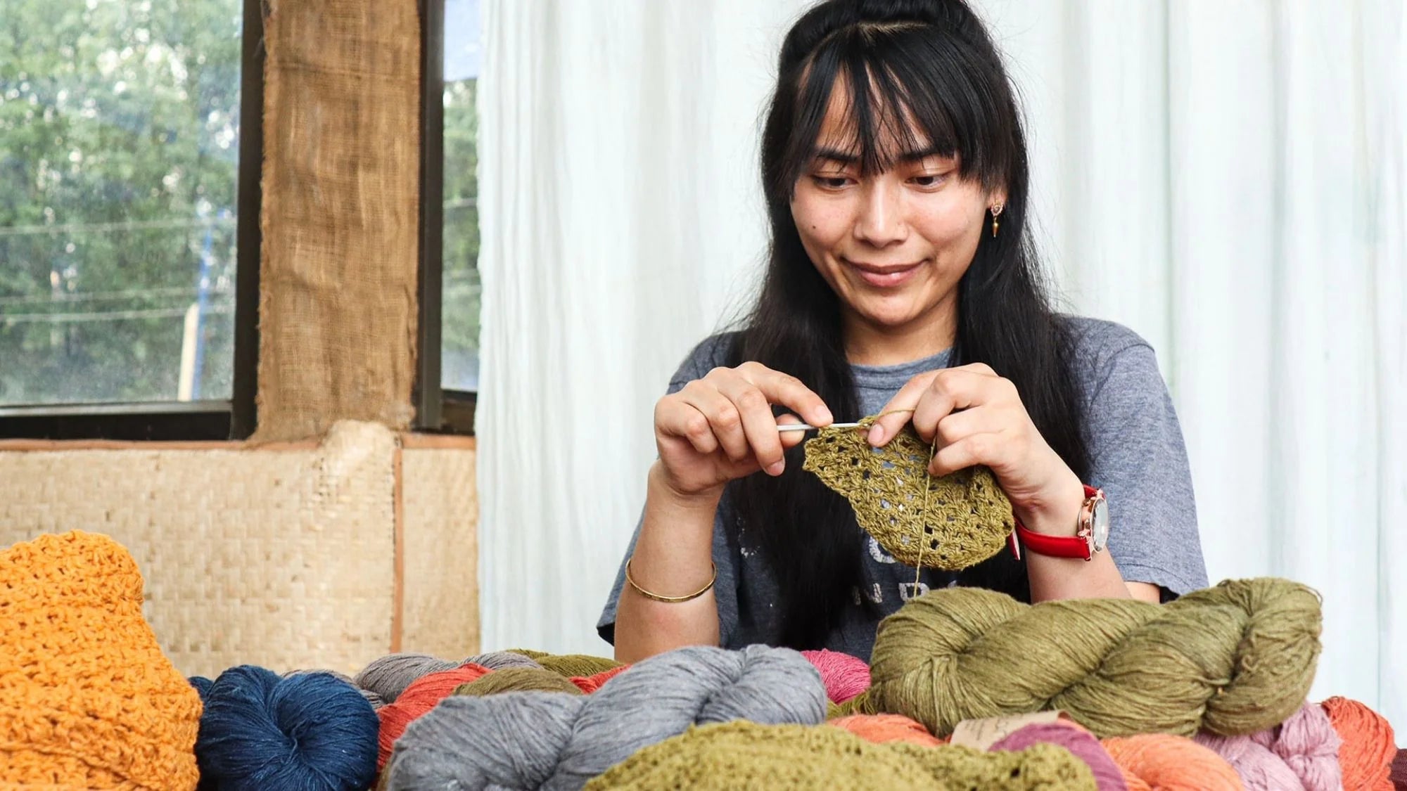 A woman knitting yarn in front of a window, showcasing her artistic skills and enjoying a peaceful moment.