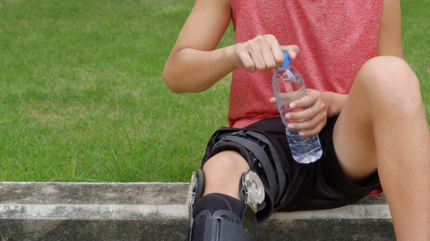 woman sitting on a bench with a knee brace taking a water break
