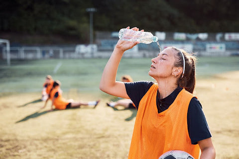 An exhausted female soccer player pouring water on her head after a soccer practice.
