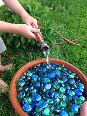 water hose filling a clay pot that has beautiful glass marbles in it for bees to stand on