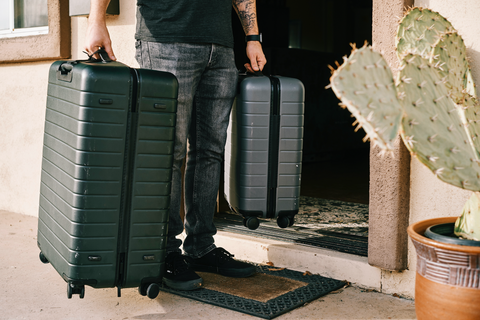 Person stepping out the front door with two black suitcases in their hands. 