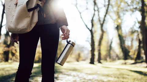 Woman with backpack carrying a reusable water bottle on a forest trail. 