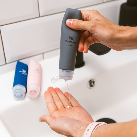 A person at a bathroom sink squeezing soap out of a silicone travel bottle onto their hand. 