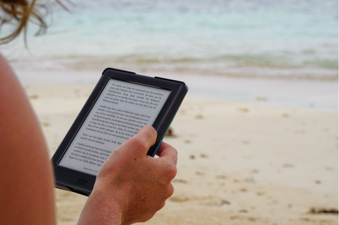 A person reading a book on a Kindle while at the beach. 