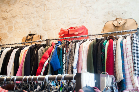 An image of a thrift store with secondhand clothing on hangers and suitcases on shelves.