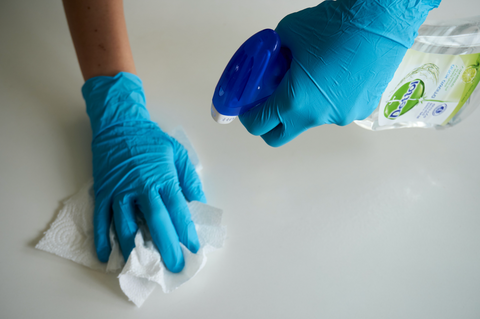A person wearing latex gloves while spraying a multi-surface cleaner on the counter. 