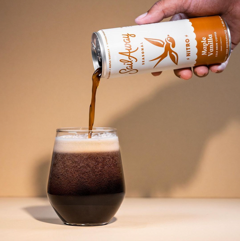 An image of Sail Away’s Maple Vanilla Cold Brew being poured out of a can into a glass on a table. 