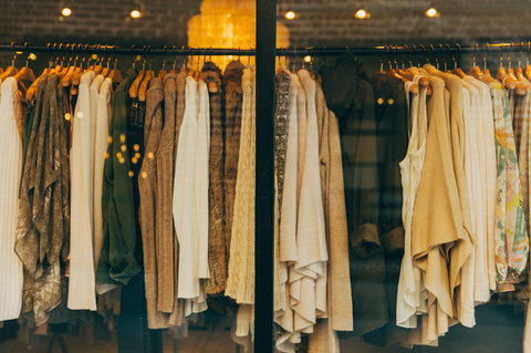 A rack of vintage and secondhand clothes inside of a thrift store window. 
