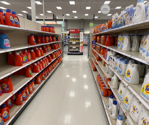 a photo of the laundry cleaning aisle in a store, with plastic containers of laundry detergent lining the shelves. 