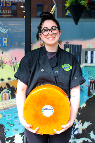 Greene Grape Provisions head cheesemonger and buyer Emilia D'Albero ACS CCP, holding a wheel of cheese in Fort Greene, Brooklyn