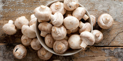 White button mushrooms in white bowl on wood table