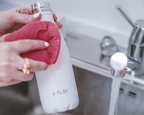 Hand washing a white bottle with a pink sponge