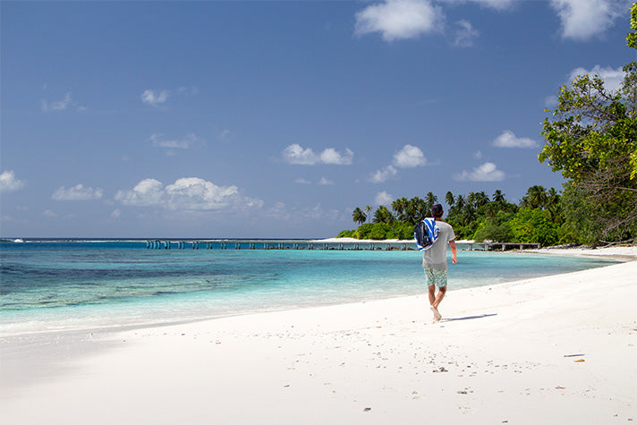 surf guide felippe dal pierro walking on a beach in the maldives wearing riz boardshorts