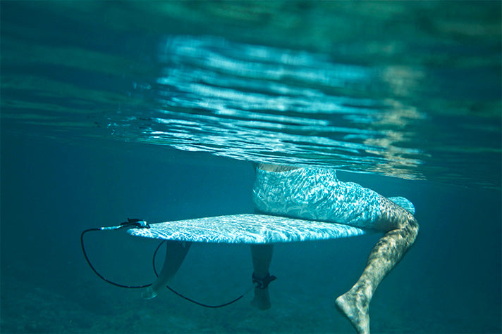 underwater view of surfer sitting on a surfboard wearing riz boardshorts